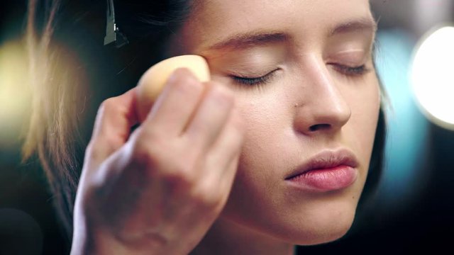 cropped view of makeup artist applying concealer around eye on model face with cosmetic sponge