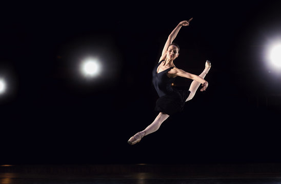 Ballerina in a black suit is jumping on a black background.