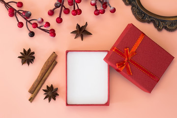 Open red gift box, cinnamon, anise star, vintage frame and holly on pink background. Top view. Christmas concept.