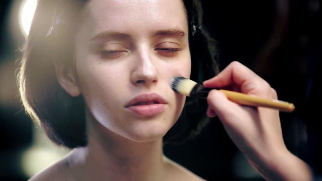 partial view of makeup artist applying primer on model face with cosmetic brush