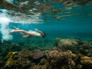 Young woman is swimming among coral reefs in shallow water.