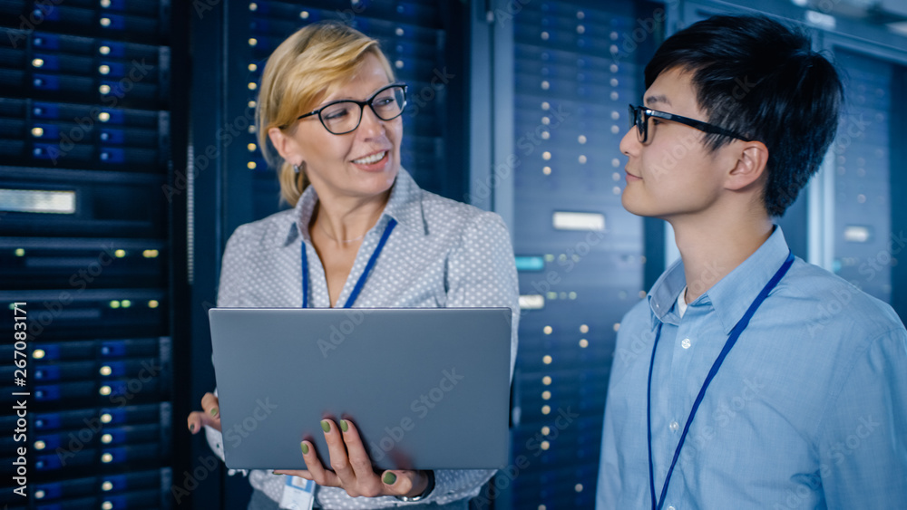 Poster In the Modern Data Center: Engineer and IT Specialist Walking alongside Server Racks, Talking, Doing System Maintenance Check with Laptop Computer. Specialists Doing Diagnostics of the Database.