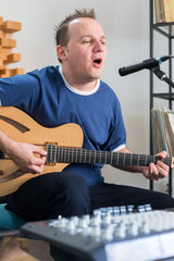 Musician singing and playing electric guitar in home music studio.