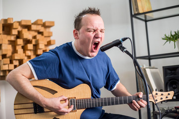 Musician singing and playing electric guitar in home music studio.