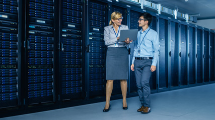 In the Modern Data Center: Engineer and IT Specialist Work with Server Racks, Talking, Doing System...