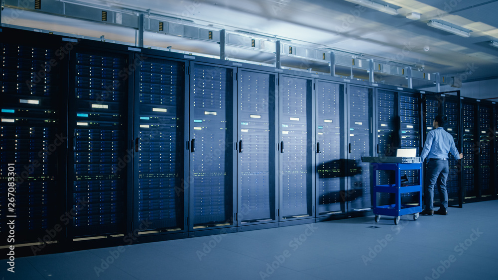Poster In the Modern Data Center: IT Engineer Doing Maintenance and Diagnostics. Pushes Cart alongside Server Racks, Opens Cabinet to Install New Hardware for Planned System Update, Equipment Replacement.