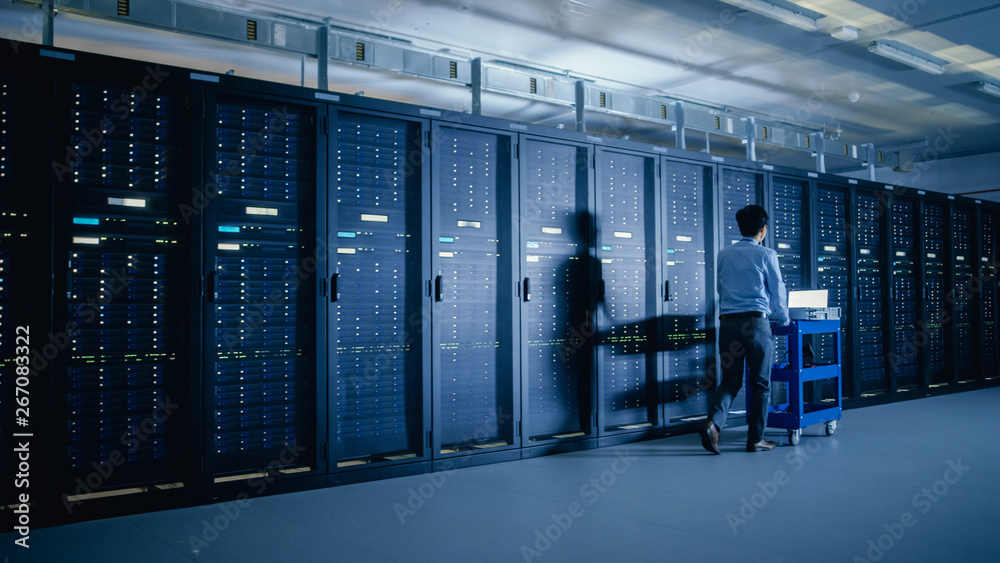 Poster In the Modern Data Center: IT Engineer Doing Maintenance and Diagnostics. Pushes Cart alongside Server Racks. Planned System Equipment Update and Maintanence.