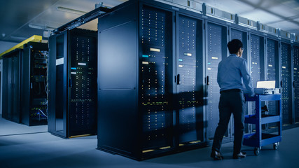 In the Modern Data Center: IT Engineer Doing Maintenance and Diagnostics. Pushes Cart alongside...