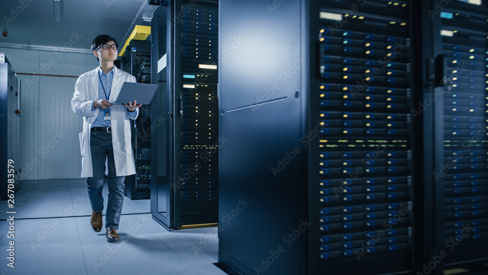 Aufkleber In Data Center: Male IT Technician Wearing White Coat Walking alongside Server Racks, Uses Laptop Computer to Run Maintenance Diagnostics Tools. He is Wearing Lab Coat and Working with Data.