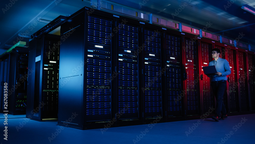 Aufkleber in data center: male it specialist walks along the row of operational server racks, uses laptop for 