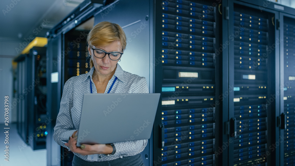 Poster Portrait Shot In Data Center: Female IT Technician Running Maintenance Programme on a Laptop, Controls Operational Server Rack Optimal Functioning. Modern High-Tech Telecommunications Data Center.