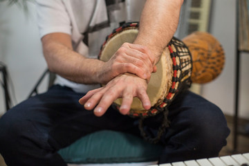Musician having wrist pain while playing djembe drum instrument in home music studio.