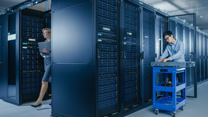 In the Modern Data Center: Team of IT Technicians Working with Server Racks, Man with Pushcart...