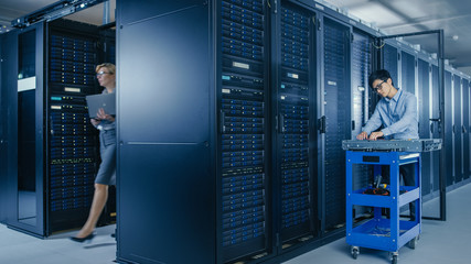 In the Modern Data Center: Team of IT Technicians Working with Server Racks, Man with Pushcart Changes Faulty Hard Drives, Doing Hardware Maintenance and Diagnostics.