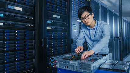 In the Modern Data Center: IT Technician Working with Server Racks, on a Pushcart Various Equipment...