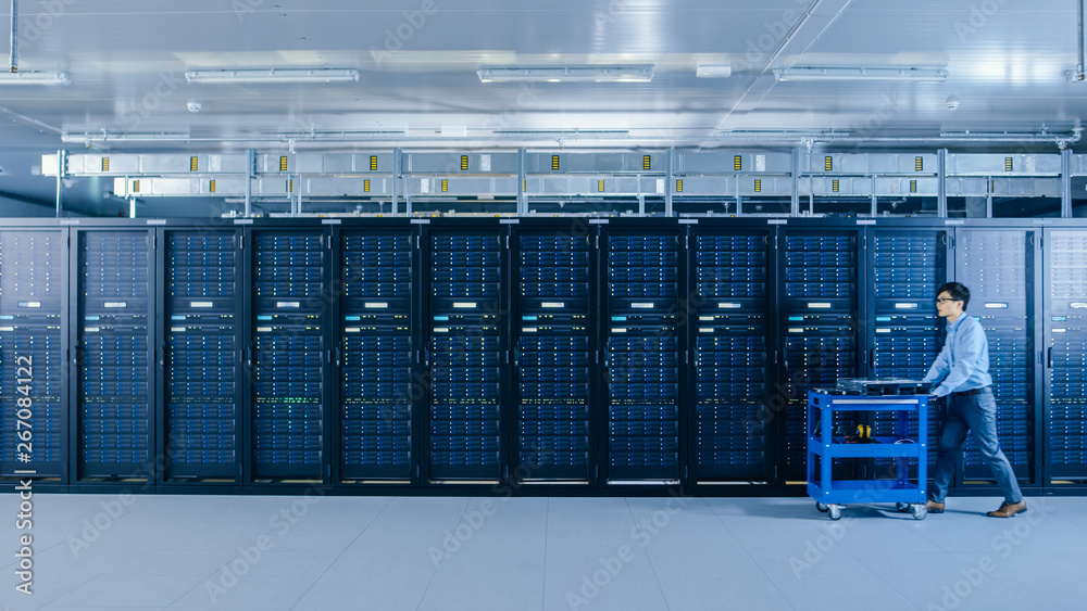 Aufkleber In the Modern Data Center: IT Technician Working with Server Racks, Pushes Cart Between Rows of Server Racks. On a Pushcart New Hardware for System Update. Engineer Doing Maintenance and Diagnostics.