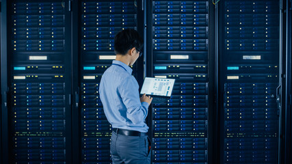 In the Modern Data Center: IT Engineer Standing Beside Open Server Rack Cabinets, Does Wireless...