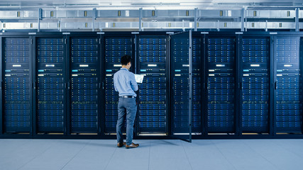 In the Modern Data Center: IT Engineer Standing Beside Open Server Rack Cabinets, Does Wireless Maintenance and Diagnostics Procedure with a Laptop.
