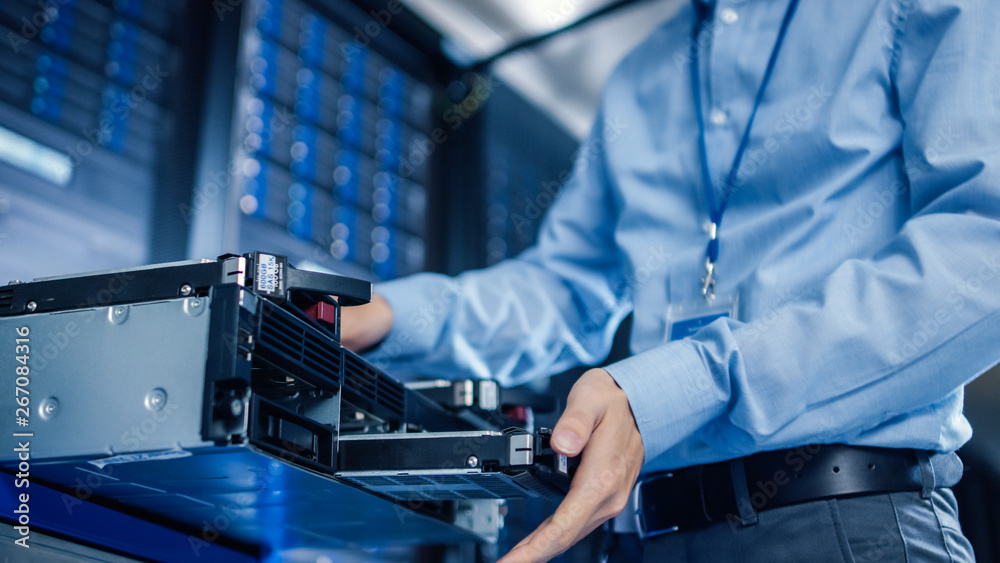 Poster In the Modern Data Center: IT Engineer Installs New HDD Hard Drive and Other Hardware into Server Rack Equipment. IT Specialist Doing Maintenance, Running Diagnostics and Updating Hardware.