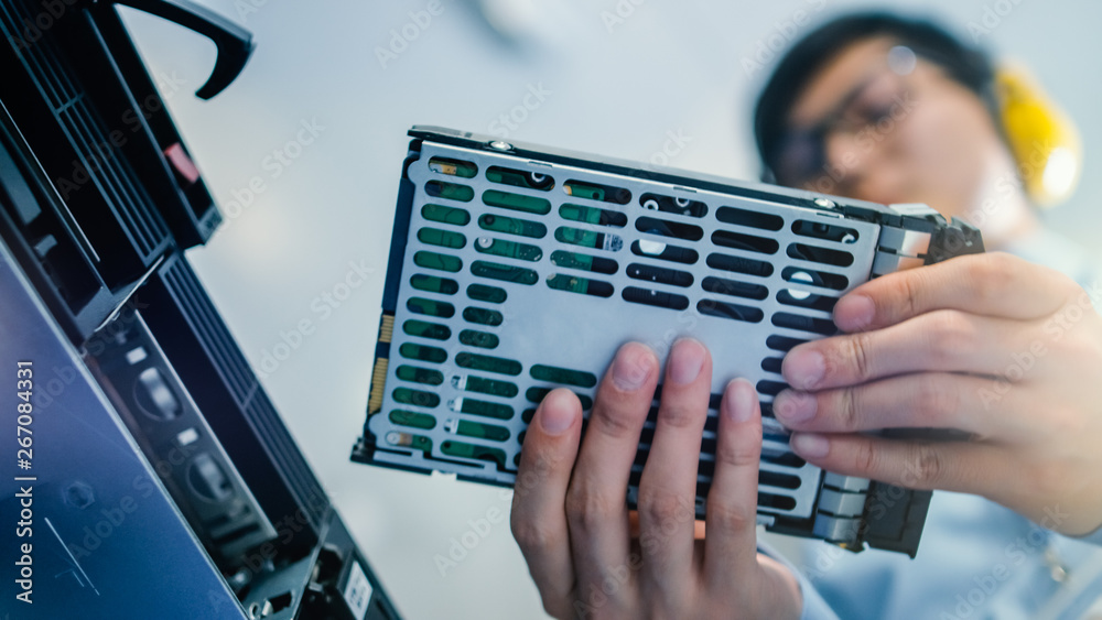 Poster In the Data Center: IT Engineer Installs New HDD Hard Drive and Other Hardware into Server Rack Equipment. IT Specialist Doing Maintenance, Running Diagnostics and Updating Hardware. Low Angle.