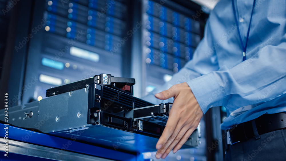 Poster In the Modern Data Center: IT Engineer Installs New HDD Hard Drive and Other Hardware into Server Rack Equipment. IT Specialist Doing Maintenance, Running Diagnostics and Updating Hardware.