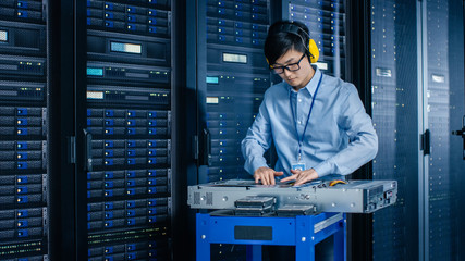 In the Modern Data Center: IT Engineer Wearing Protective Muffs Installs New Hardware for Server Rack. IT Specialist Doing Maintenance, Updating Hardware for Stable Functioning of Database System.