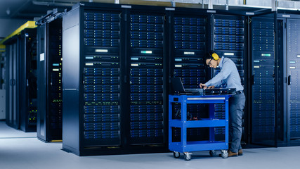 In Data Center: IT Engineer Wearing Protective Muffs Installs New Hardware for Server Rack....