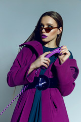 Obraz premium beautiful spectacular long-haired girl in sunglasses and a bright coat holding a lilac phone in hand. Disk phone