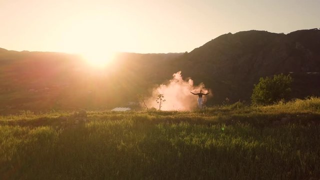 Silhouette di una ragazza con fumogeni colorati, mentre danza in cima alla montagna al tramonto.