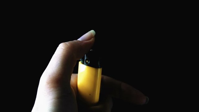The girl holds a yellow lighter. She lights the flame. Black background, close-up.