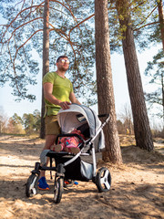 Young attractive father walks in the summer with a stroller on the sandy beach near the sea. Dad walks with his daughter. Caring young father