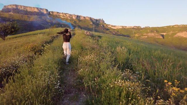 Ragazza balla su una strada sterrata in cima alla collina in campagna al tramonto.