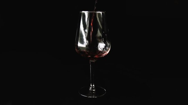 big glass on a dark background. Red wine is slowly poured into a glass.
