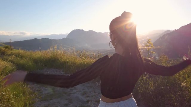 Ragazza con tuta grigia e maglia nera balla a ritmo di musica in mezzo a una strada in campagna tra la natura. Tramonto del sole sullo sfondo.