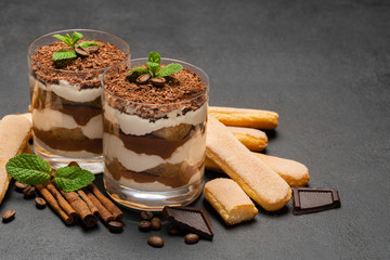 Classic tiramisu dessert in a glass and savoiardi cookies on dark concrete background