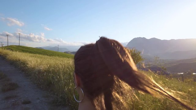 Ragazza con tuta grigia e maglia nera balla a ritmo di musica in mezzo a una strada in campagna tra la natura. Tramonto del sole sullo sfondo.