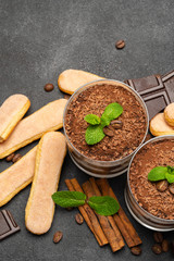 Classic tiramisu dessert in a glass and savoiardi cookies on dark concrete background