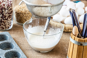 Flour is sifted through a sieve into a glass bowl of milk.