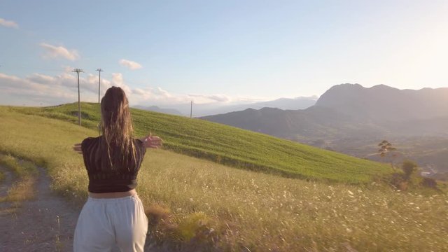 Ragazza con tuta grigia e maglia nera balla a ritmo di musica in mezzo a una strada in campagna tra la natura. Tramonto del sole sullo sfondo.