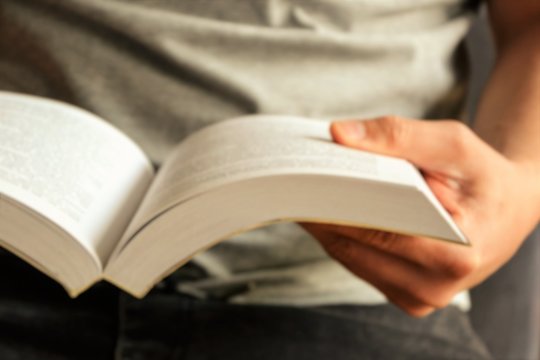 Man is reading a book, close up, vintage style. Book opened for reading. Young man is reading a book.Close-up picture of hand holding a book. Out of focus, intentionally blurred