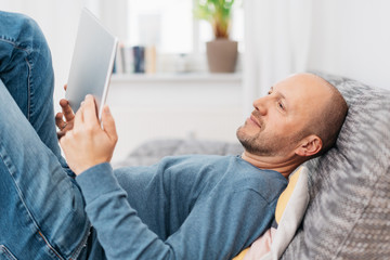 Man relaxing on a couch reading on a tablet pc