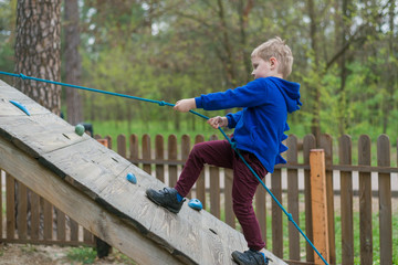 A little boy is training in a rope park. The child climbs the obstacle course. Active recreation in the park in the fresh air.