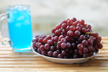 Purple grapes placed in a white plate on a bamboo table, blurred background.
