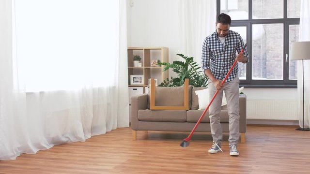 cleaning, housework and housekeeping concept - indian man with broom sweeping floor at home