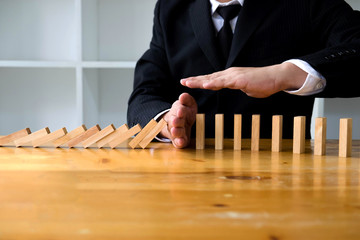 Business hand stops domino continuous overturned meaning that hindered business failure. Stop over...