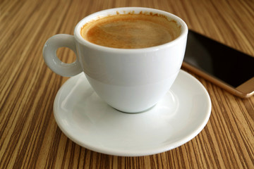 One Cup of Hot Black Coffee with a Blurry Cellphone in Background