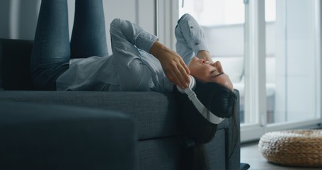Portrait of an young woman is lying on the sofa and having fun listening to the music with wireless...