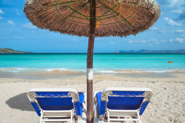 Two Beach loungers under a parasol at the turquoise sea