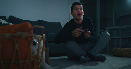 Portrait of an young man having fun to play a video games in living room in the evening.