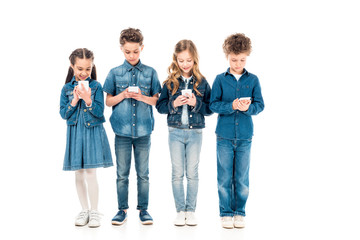 Fototapeta premium full length view of four kids in denim clothes using smartphones isolated on white